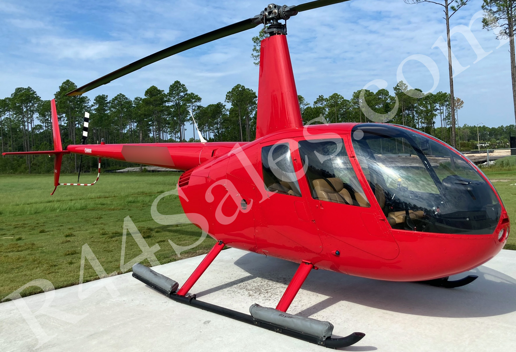 A red Robinson R44 on a concrete pad in the Florida pines